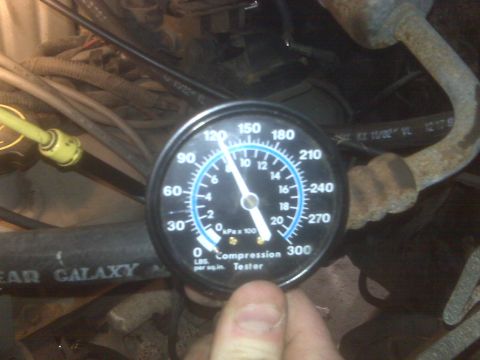 1995 Ford Bronco - A close-up view of a compression tester gauge inserted into an engine bay. The gauge needle is pointing to approximately 120 PSI, indicatin…