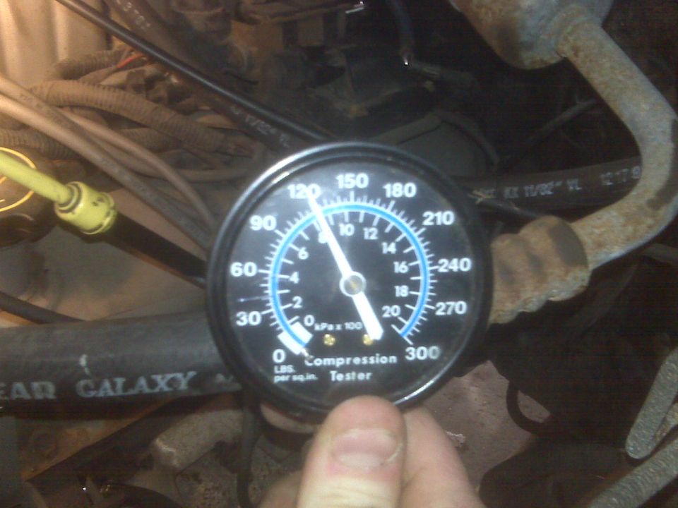 Compression tester gauge showing 120 PSI in an engine bay.