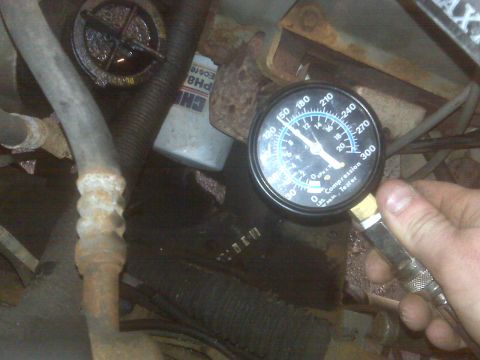 1995 Ford Bronco - A hand holds a compression tester gauge connected to an engine bay. The gauge reads approximately 130 PSI.