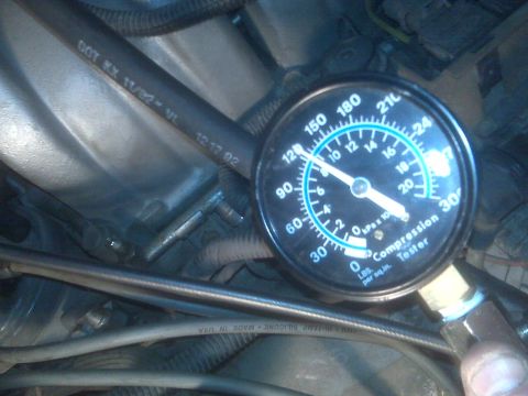 1995 Ford Bronco - A close-up view of a compression tester gauge connected to an engine bay. The gauge shows a reading between 150 and 180 PSI, with the needl…