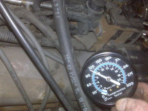 1995 Ford Bronco - A close-up view of a compression tester gauge being held in front of engine components. The gauge reads approximately 110 PSI or 750 kPa x…