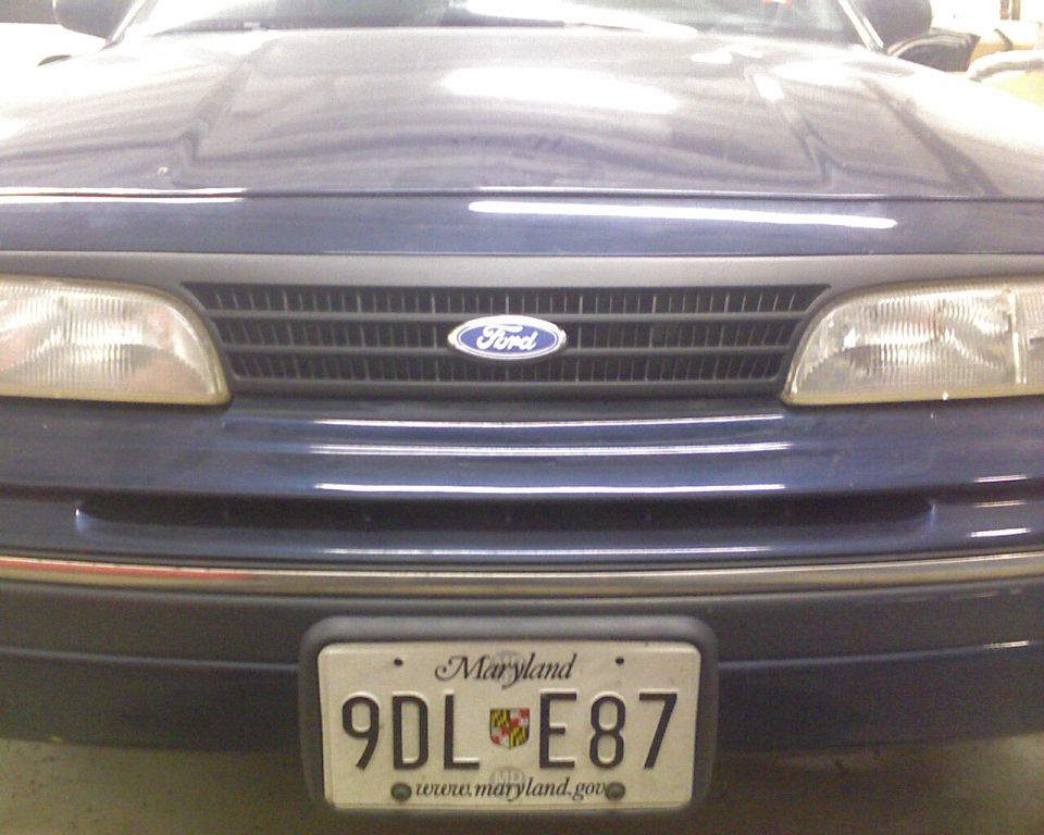 Front grille and bumper of a dark blue Ford sedan with Maryland plate 9DL E87 in a garage