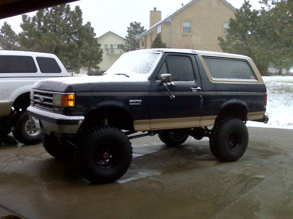Lifted dark blue and tan Ford Bronco with large tires in the snow.