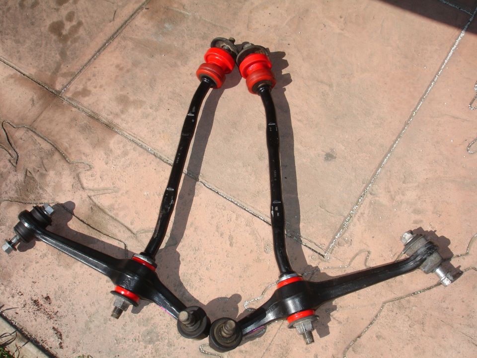 Two black control arms with red polyurethane bushings on pavement