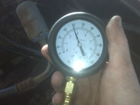 1995 Ford Bronco - A hand holds a pressure gauge with a needle pointing to approximately 40 PSI, with a blurry engine bay in the background.