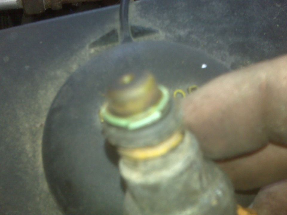 Hand holding a fuel injector with a green O-ring over a dark engine part.