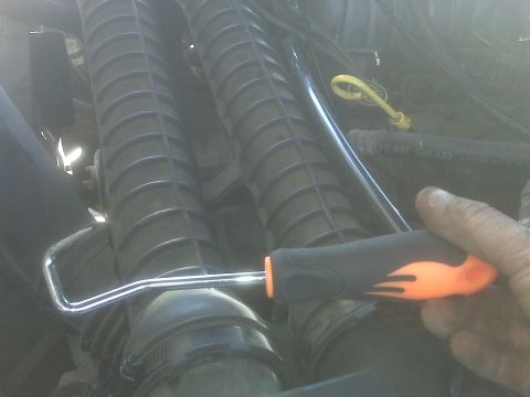 1995 Ford Bronco - A hand holds an orange and black handled tool with a metal U-shaped end, positioned over a ribbed black plastic component of an engine. The…