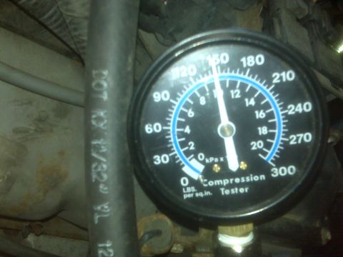 1995 Ford Bronco - A close-up of a compression tester gauge with the needle pointing between 120 and 150 psi. The gauge is connected to a black hose with whit…