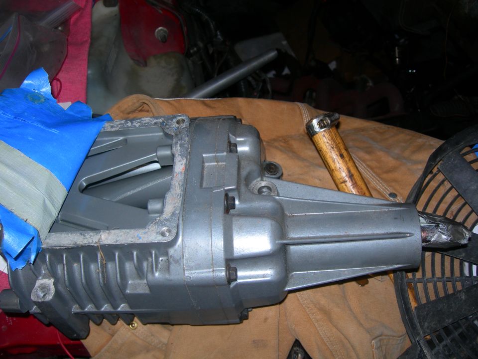 Gray supercharger with blue tape, resting on a brown cloth. A hammer handle is visible
