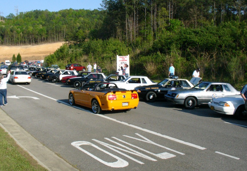 Orange convertible Mustang and several police cars parked on a road.