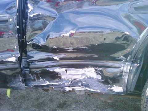 1972 Ford Ranchero - Close-up of severe collision damage down the side of a black vehicle: the front fender, door skin and rocker panel are crushed and creased…