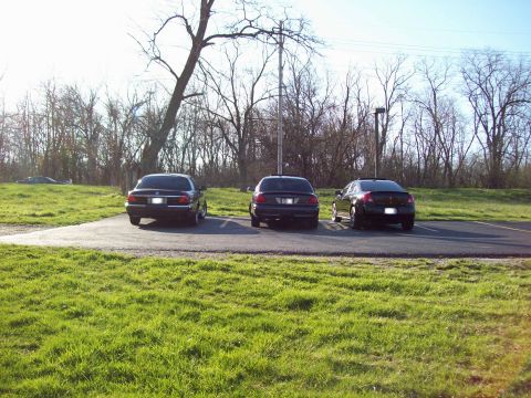 1999 Mercury Grand Marquis - Three sedans are parked in a lot next to a grassy area. The car in the middle appears to be a dark color, possibly black or dark blue.