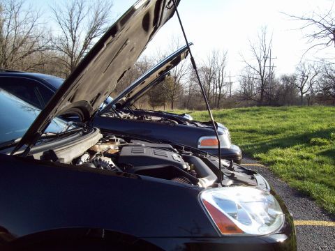1999 Mercury Grand Marquis - Two black sedans with their hoods open are parked side-by-side on a gravel shoulder next to a grassy field. The front car's engine and head…