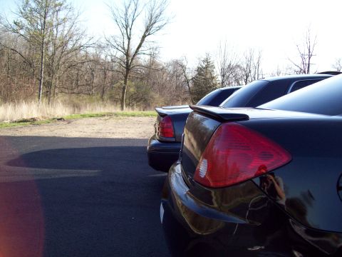 1999 Mercury Grand Marquis - The rear passenger side of a black sedan is shown in the foreground, with the taillight and spoiler clearly visible. Two other dark-colored…