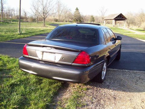 1999 Mercury Grand Marquis - The rear passenger side of a dark gray sedan is shown parked on the side of a paved road. A wooden picnic shelter is visible in the backgro…