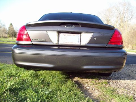 1999 Mercury Grand Marquis - The rear view of a dark gray sedan parked on grass with a gravel shoulder. The car has a spoiler and an Illinois license plate.