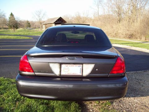 1999 Mercury Grand Marquis - The rear view of a dark gray sedan is shown parked on a grassy area next to a paved surface. The license plate is visible and reads "20 ILL…