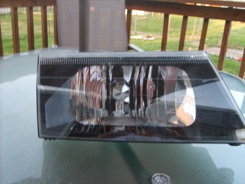 1993 Ford Crown Victoria - A black aftermarket headlight assembly is displayed on a glass table outdoors. The headlight is angled slightly to the right, showing its r…
