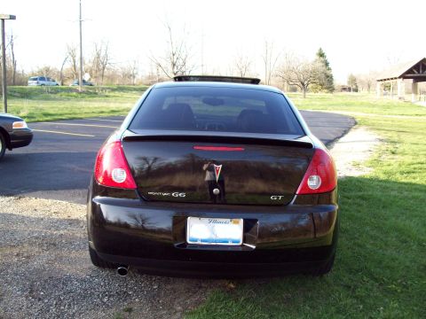 1999 Mercury Grand Marquis - The rear of a black Pontiac G6 GT sedan is shown parked on a gravel surface next to a grassy area. The car has a spoiler and an Illinois li…