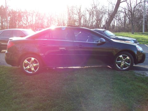 1999 Mercury Grand Marquis - A dark colored sedan is parked on a grassy area next to a paved surface. The car is viewed from the side with the sun glinting off the pain…