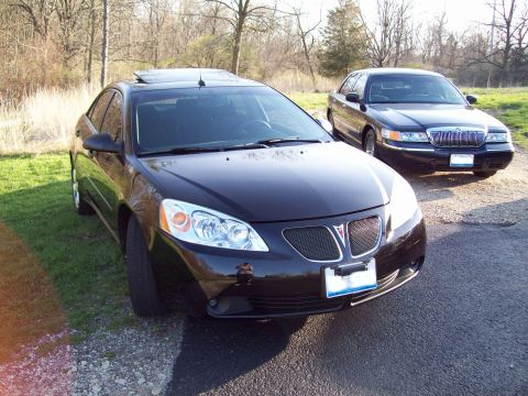 1999 Mercury Grand Marquis - Two black sedans are parked on a gravel and asphalt driveway next to a grassy area with trees in the background. The car in the foreground…
