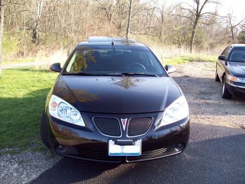1999 Mercury Grand Marquis - The front view of a black sedan is shown parked on an asphalt driveway next to a grassy area and trees. A second dark-colored sedan is part…