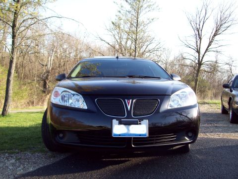 1999 Mercury Grand Marquis - Front view of a black Pontiac G6 sedan parked on an asphalt surface with a grassy area and trees in the background. The car features a chro…