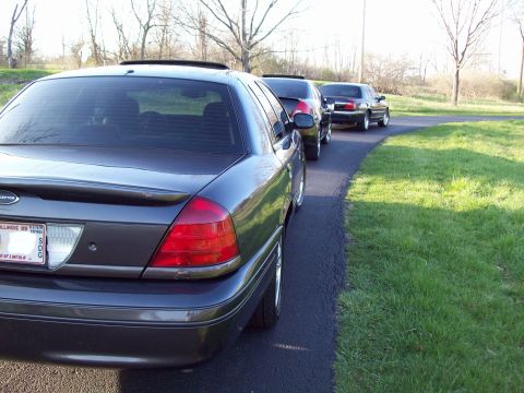 1999 Mercury Grand Marquis - The rear passenger side view of a dark gray sedan parked on an asphalt driveway next to a grassy area. The car has tinted windows and a spo…