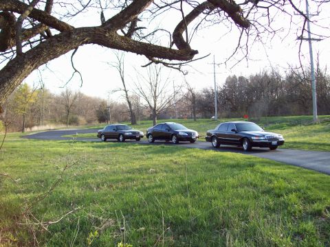 1999 Mercury Grand Marquis - Three dark-colored sedans are parked on a paved road in a grassy, tree-lined area. The vehicle in the foreground is a Mercury Grand Marquis…