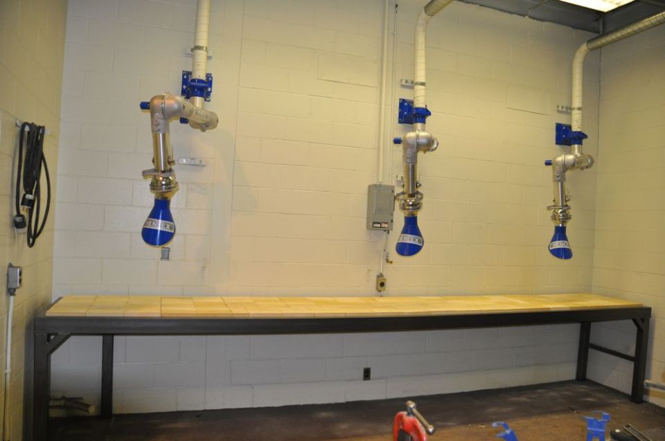 Three blue fume-extraction arms mounted over a long shop workbench