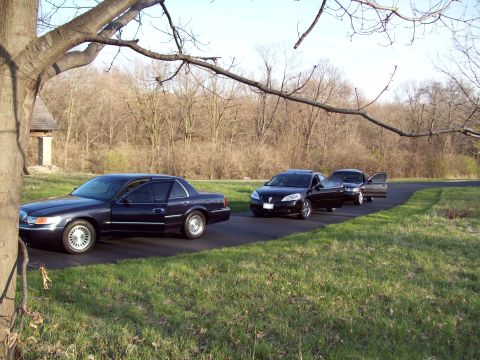 1999 Mercury Grand Marquis - A dark blue sedan parked on a paved driveway next to a grassy area with trees in the background. The driver's side front and rear doors are…
