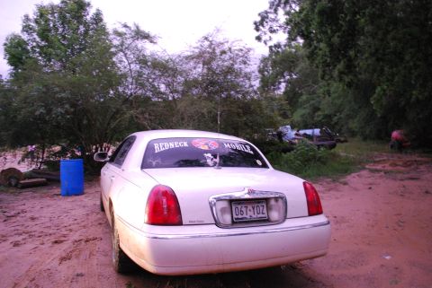 2008 Jeep Wrangler - The rear of a white sedan is shown parked on a dirt road. The car has a license plate that reads "067-YDZ" and a sticker on the rear window…