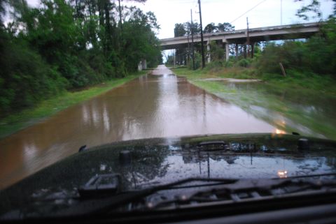 2008 Jeep Wrangler - A flooded road is seen from the perspective of a vehicle's interior, with trees and an overpass visible in the background.