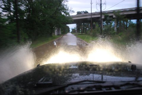 2008 Jeep Wrangler - The front view of a vehicle driving through flooded conditions, with water splashing high on either side of the headlights. An overpass is…