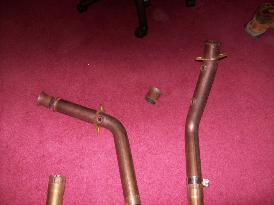 Close-up of three bent metal exhaust pipes against a red background