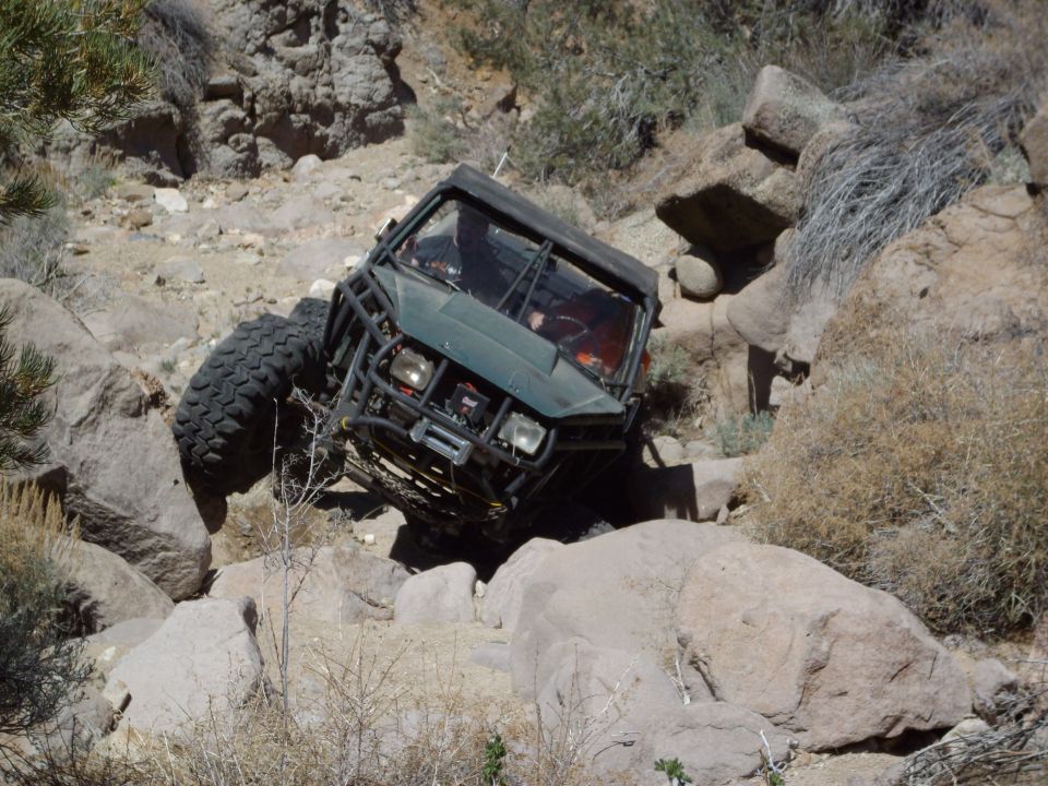 Green off-road vehicle with roll cage climbing over rocks.