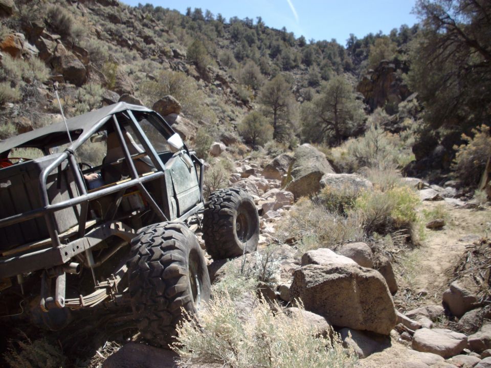 Off-road vehicle with roll cage on a rocky mountain trail.