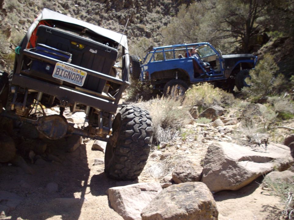 Two off-road vehicles on a rocky trail. One is a modified SUV, the other is a blue off-road vehicle.