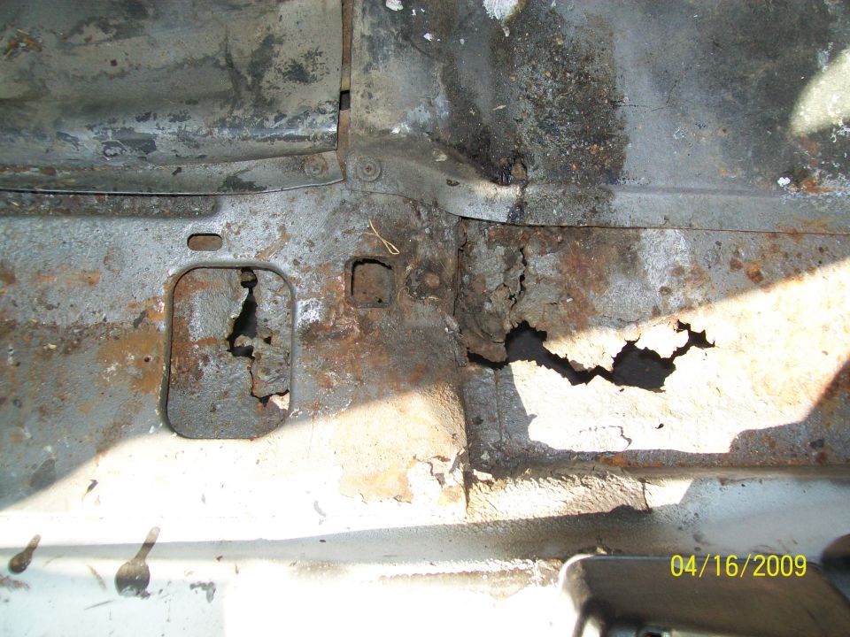 Close-up of severe rust and holes in a vehicle floor pan.