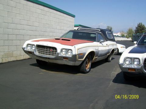1972 Ford Ranchero - A white and red 1972 Ford Ranchero is parked in front of a cinder block building. The vehicle has a black camper shell and is seen from a f…