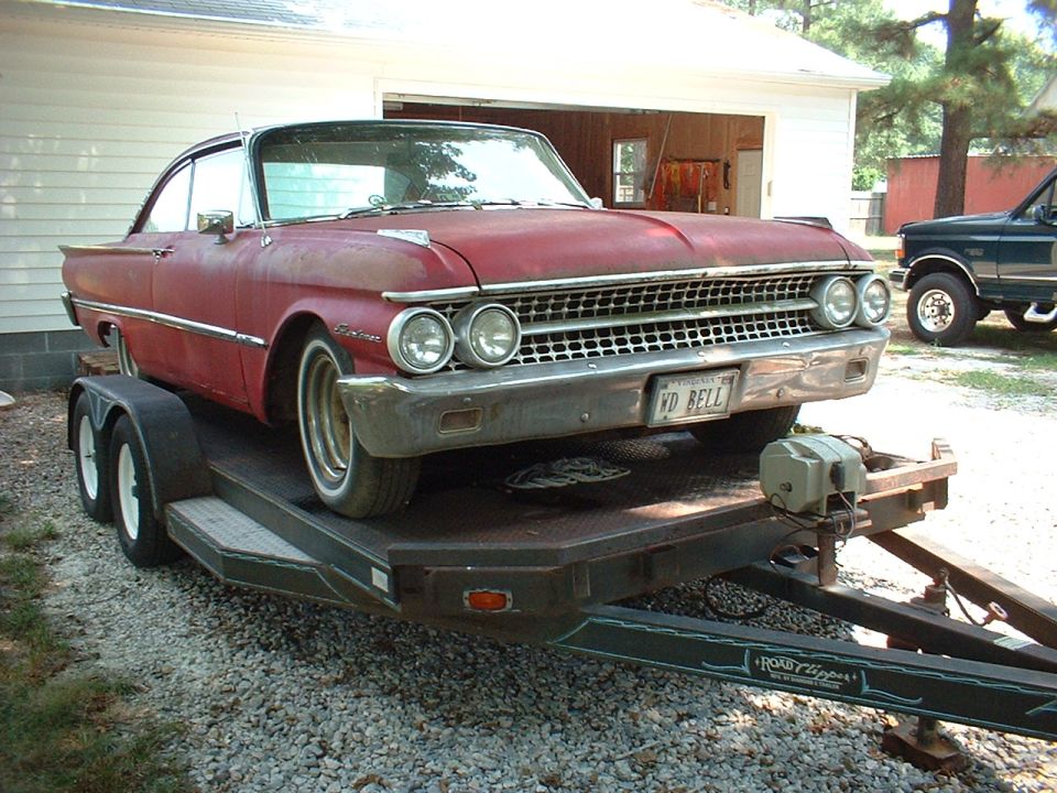 Faded red vintage Ford hardtop coupe on a black flatbed trailer, front 3/4 view