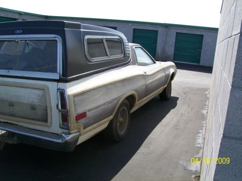 1972 Ford Ranchero - The rear passenger side of a white 1972 Ford Ranchero with a dark camper shell is parked next to a concrete building with green garage door…