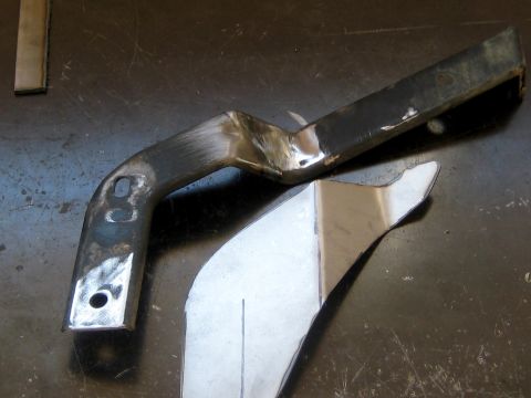 1996 Ford Bronco - Two custom fabricated metal parts are shown on a dark, scratched surface. One part is a bent, black metal bracket with holes and evidence o…