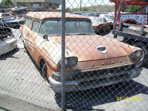 1972 Ford Ranchero - A rusty, orange station wagon is parked behind a chain-link fence. The car appears to be from the 1950s and is in a state of disrepair.