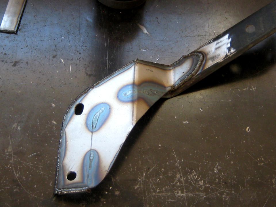 Fabricated steel bracket with blue weld heat coloring and two bolt holes on a shop table