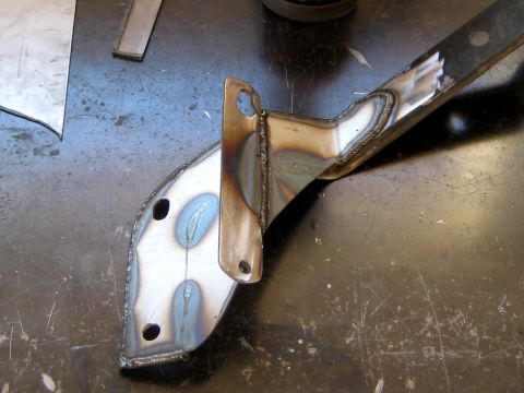 1996 Ford Bronco - A close-up, angled view of a welded metal bracket with visible heat discoloration and two circular holes. The bracket appears to be part of…