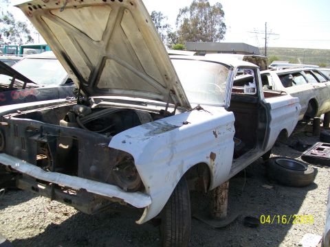 1972 Ford Ranchero - A white, two-door vehicle with its hood open is parked in an outdoor lot with other vehicles. The front end of the vehicle is missing its g…