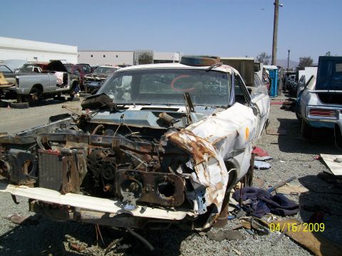 1972 Ford Ranchero - A heavily damaged and rusted 1972 Ford Ranchero is shown in a junkyard setting. The front end is missing, revealing the engine bay and radi…