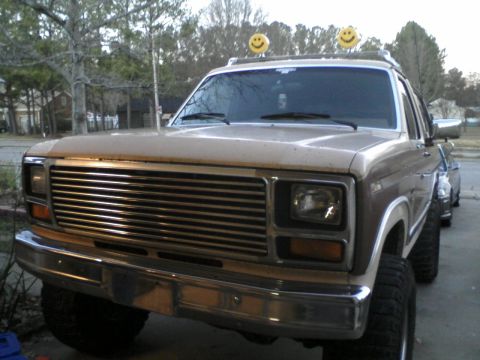 1986 Ford Bronco - This tan SUV, seen from a 3/4 front angle, features decorative smiley face lights on its roof rack.