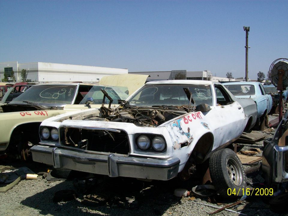 White 1975 Ford Ranchero front view, hood open, in junkyard